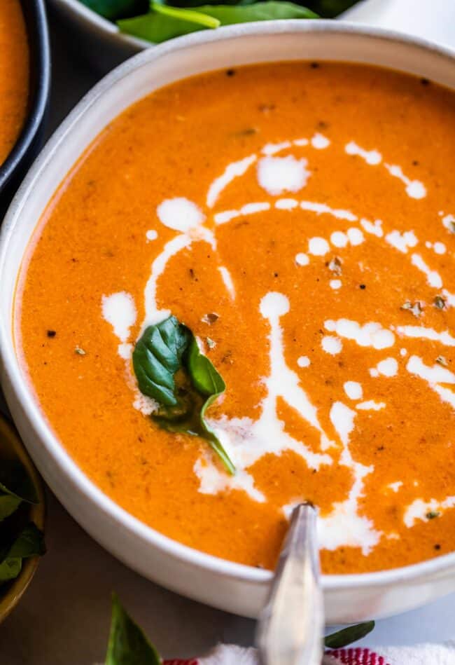 cream drizzled on creamy tomato soup with fresh basil in a bowl. 