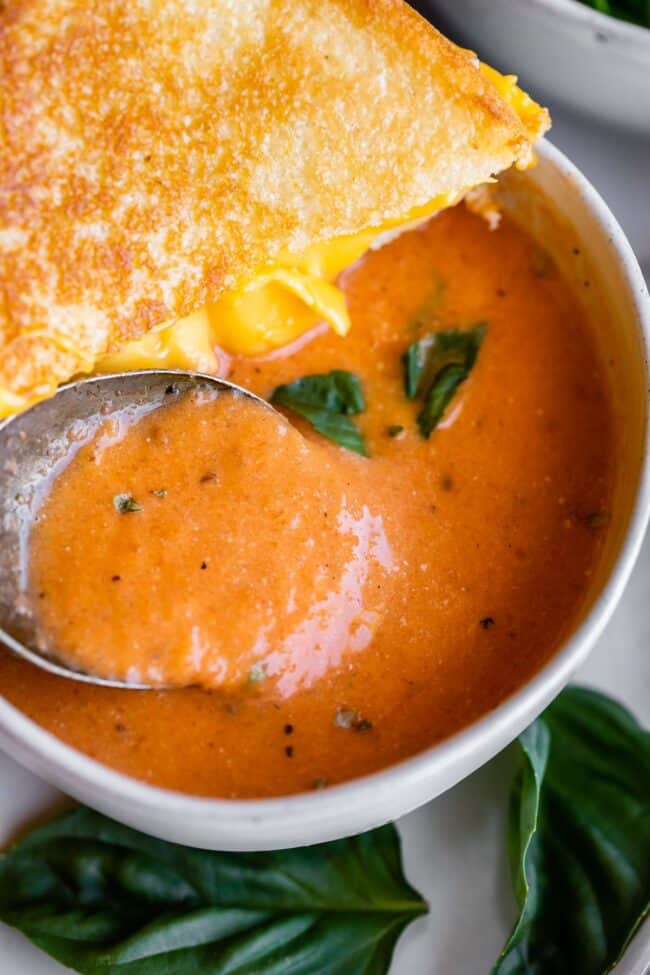 Quick tomato soup in a white bowl with half a grilled cheese sandwich balanced on top.