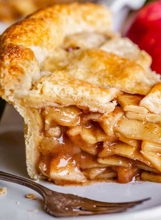 a thick slice of apple pie with a fork on a white plate.
