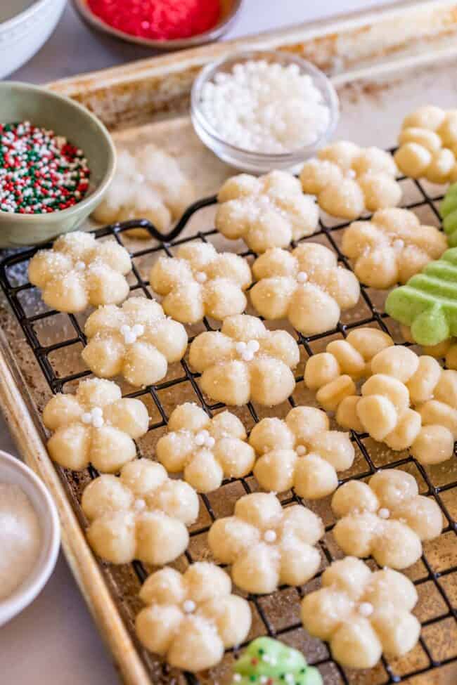 spritz cookies laid out on a cooling rack, ready to decorate with sprinkles.