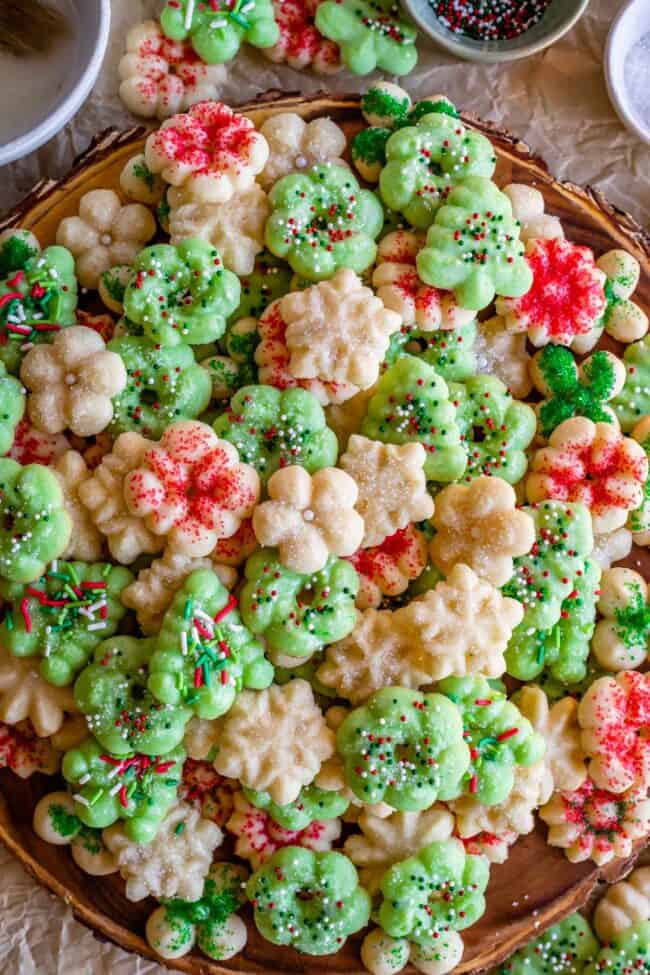 dozens of buttery spritz cookies laid out on a board, decorated with sprinkles.