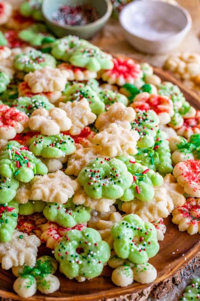 buttery Christmas spritz cookies laid out on a wooden board with sprinkles.