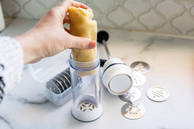 adding a cylinder of spritz cookie dough to a cookie press.