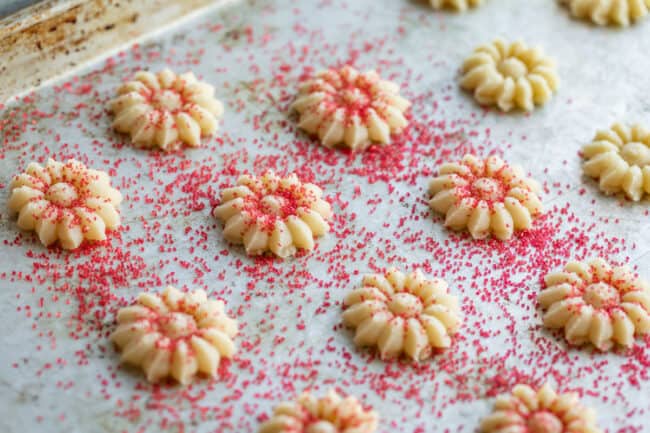 shaped cookie dough lined up on a pan with red sanding sugar sprinkled on top