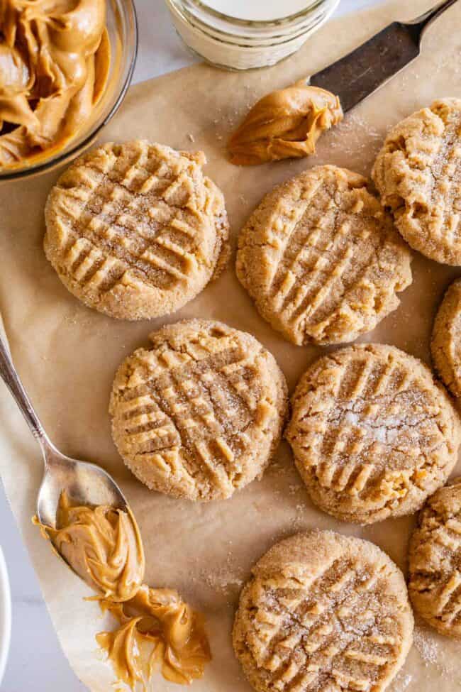 peanut butter cookies on a sheet of brown parchment paper with a spoonful of peanut butter.