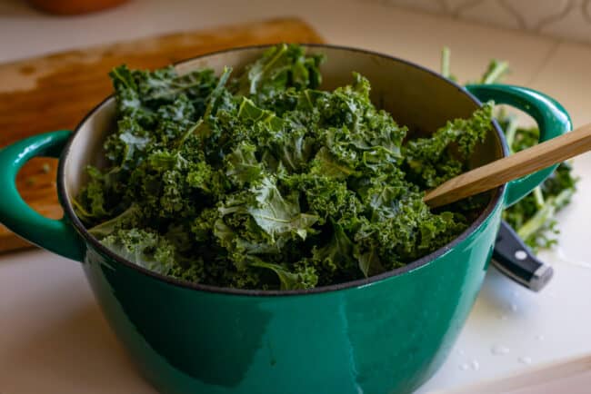 lots of kale in a big teal pot of soup
