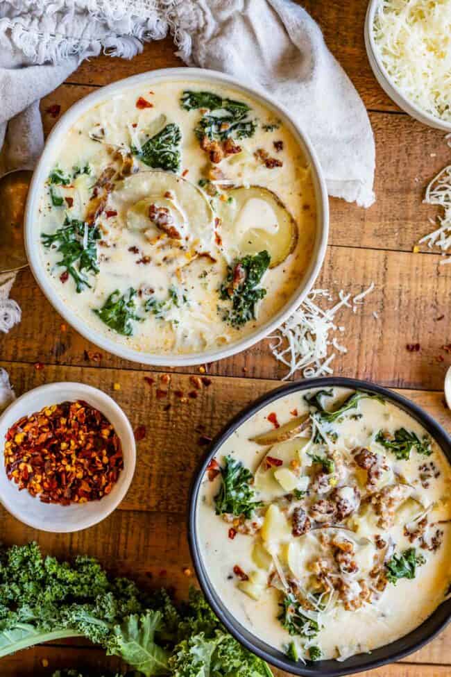 sausage kale soup in a white bowl and black bowl on a wooden board with parmesan