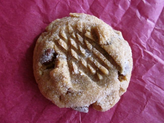 peanut butter cookie with chocolate chips and fork hash marks on top of cookie on red tissue paper.