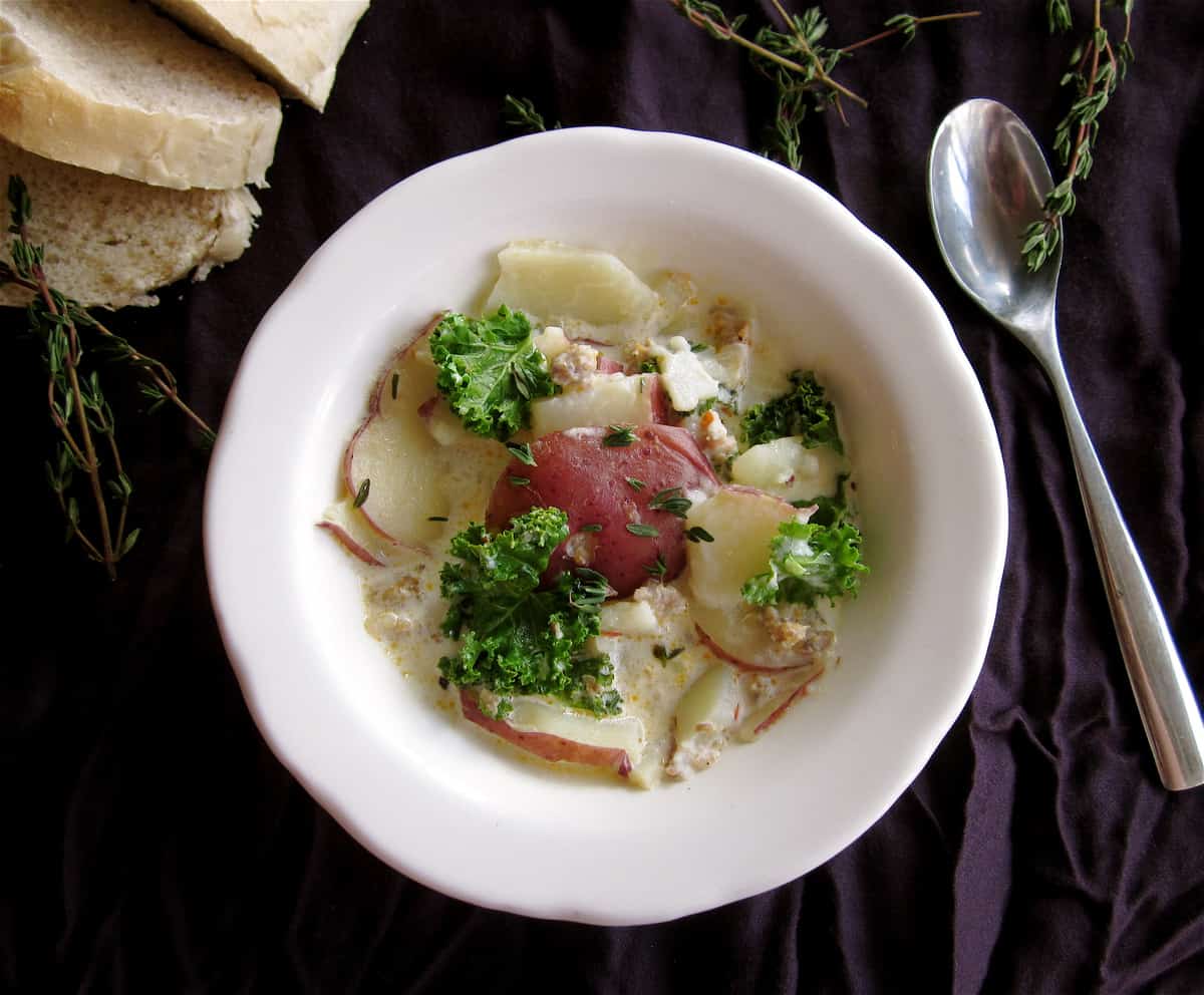 Sausage Potato & Kale Soup in a white bowl with spoon and purple napkin