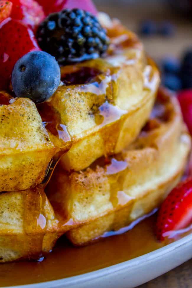 a stack of homemade waffles on a plate covered in syrup and topped with fresh berries. 