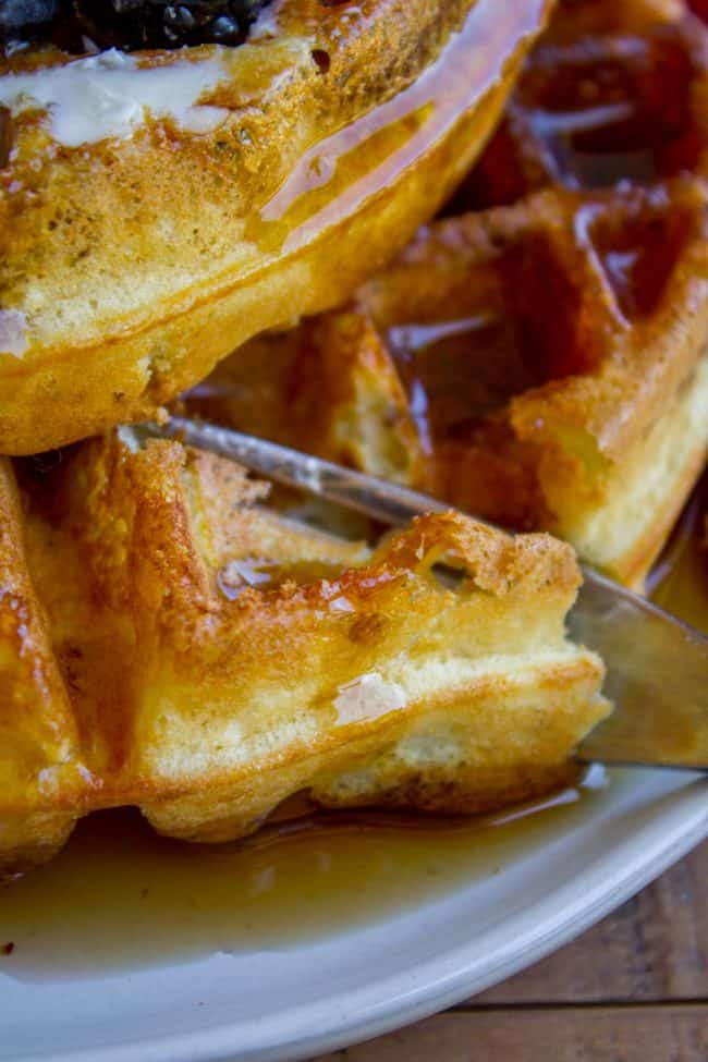 a fork cutting into a stack of homemade syrup covered waffles.