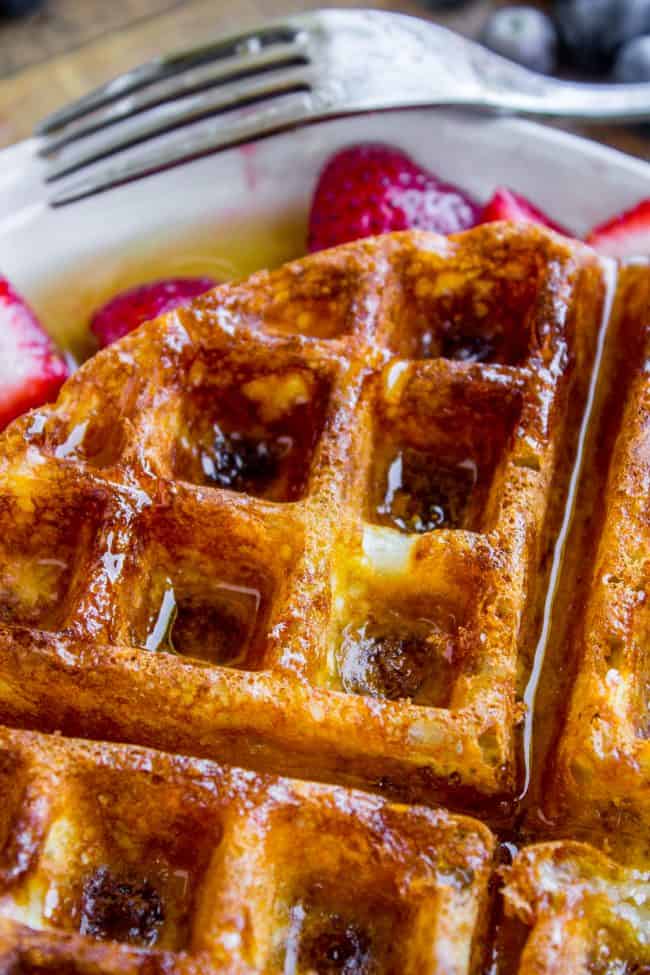 homemade waffles on a plate with syrup and strawberries.