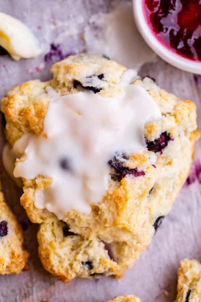 scone with glaze on top on parchment paper with jam nearby.