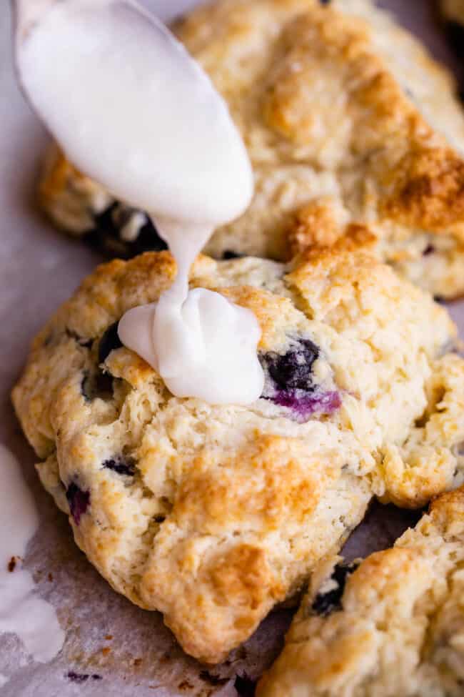 drizzling glaze onto a blueberry scones from a spoon.