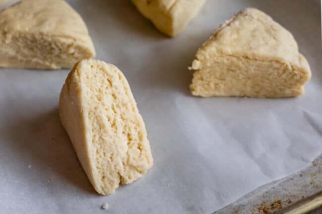 unbaked scones with flaky layers waiting to be baked on parchment paper lined baking sheet.