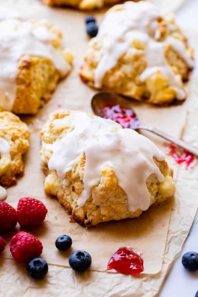 glazed scones on a baking sheet with fresh fruit nearby and a jelly spoon between them.