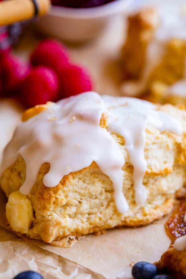 glazed scone on parchment paper with blueberries nearby.