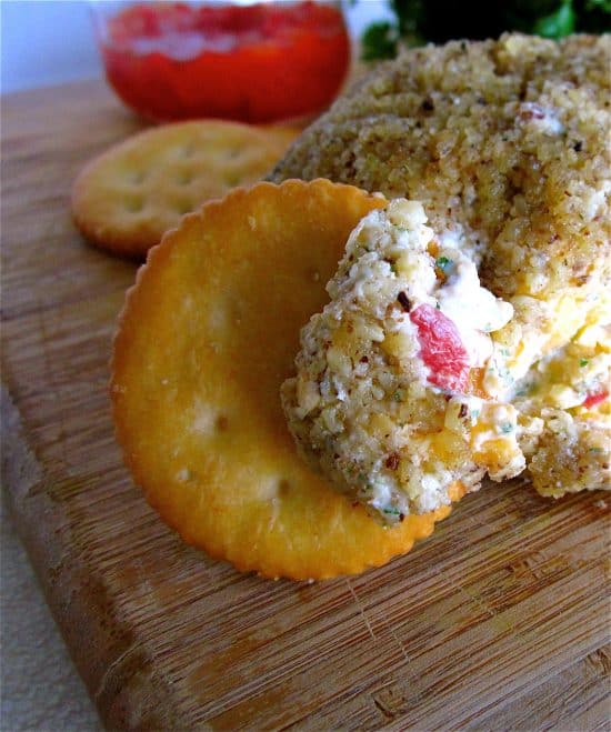 Buttery cracker dipped in pimiento cheeseball on cutting board.