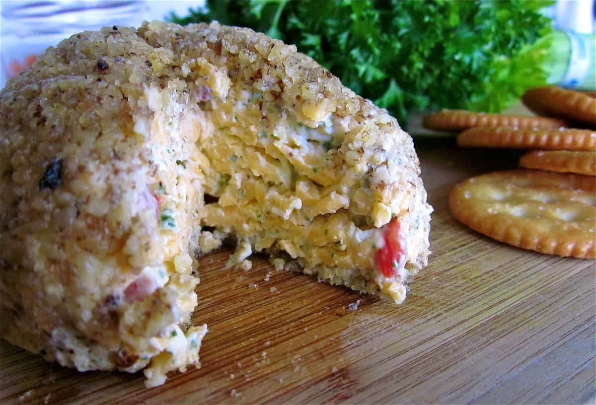 Pimiento cheese ball with slice cut out on cutting board.