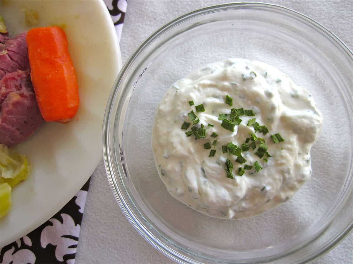 an old photo of a bowl of horseradish sauce near a plate of corned beef, cabbage, and carrots.