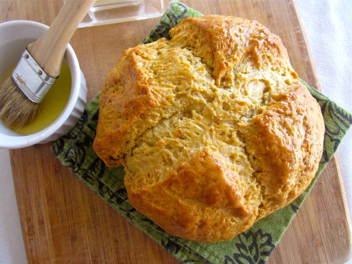 Irish soda bread on a wooden cutting board with melted butter on the side. 