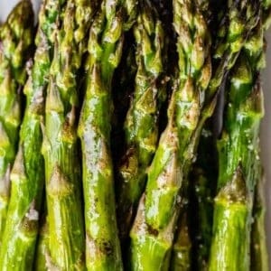 Close-up of oven roasted asparagus spears on a white plate, glistening with oil and sprinkled with coarse salt.