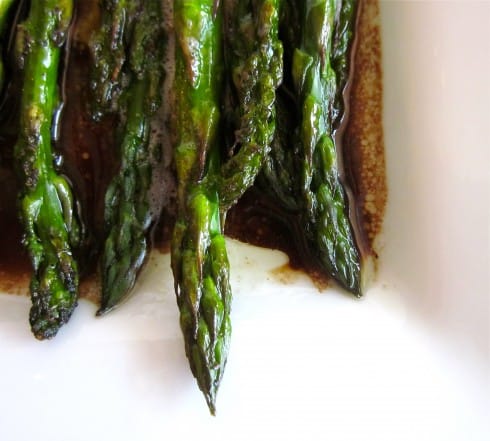 close-up of ends of oven roasted asparagus on white plate with balsamic glaze.