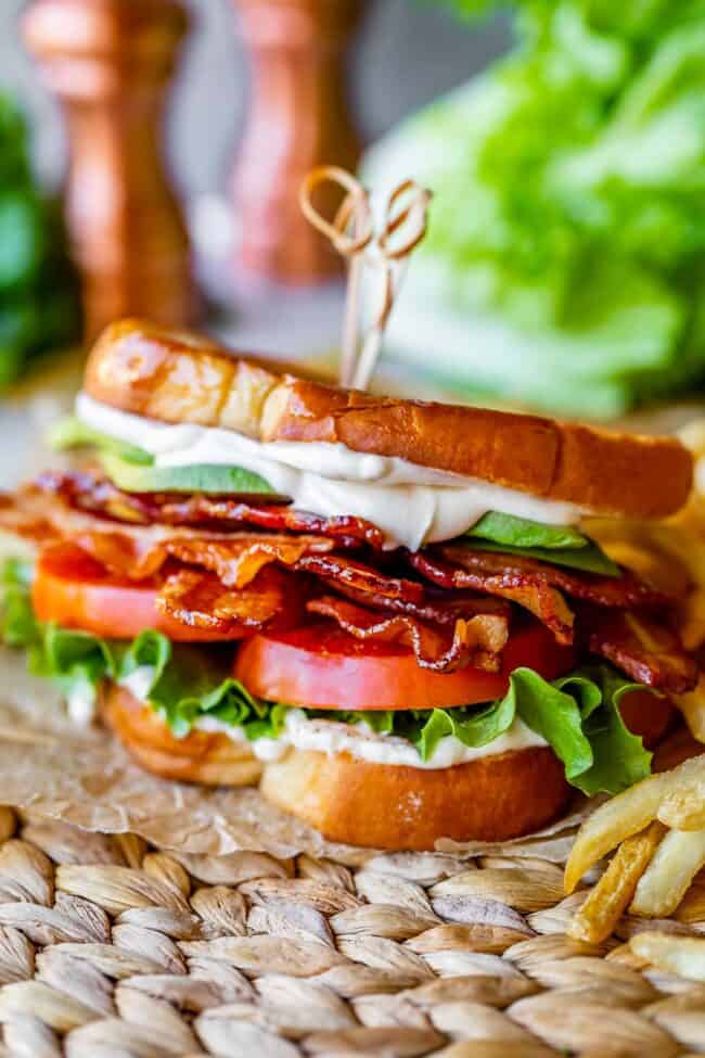 blt sandwich with french fries, on parchment paper with lettuce and salt and pepper shakers in the background