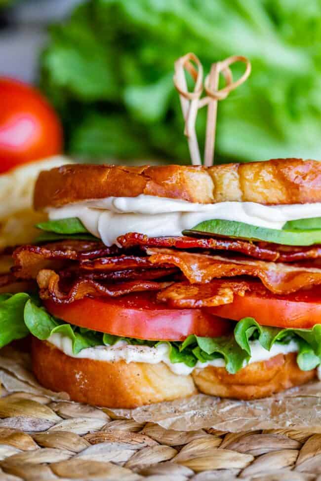 avocado BLT with toothpicks on top, on parchment paper with lettuce in the background