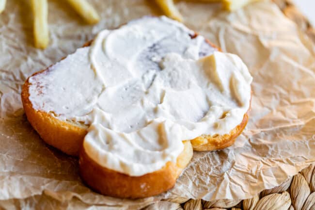 mayonnaise on white bread on parchment paper with fries in the background