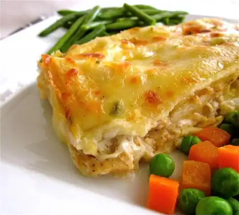 A slice of creamy lasagna topped with melted cheese, served on a white plate alongside green beans, peas, and diced carrots—perfect for fans of comforting classics like Chicken Crepe Casserole.