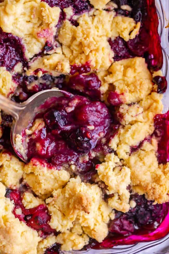 berry cobbler recipe in a pan with a metal spoon.