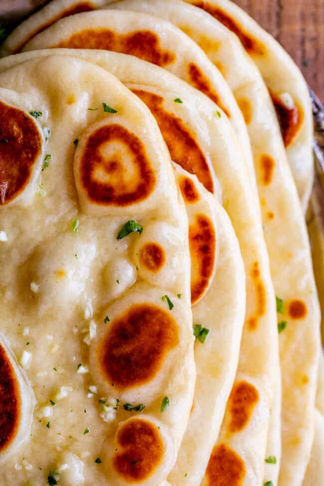 buttered homemade naan with garlic and fresh parsley stacked up, shot from above.