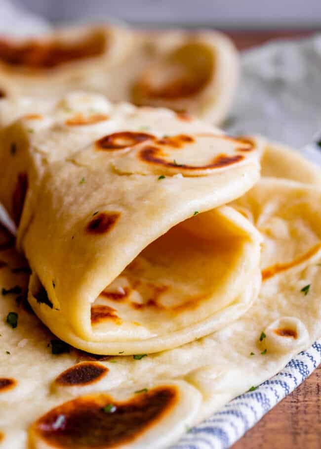 homemade naan bread rolled up on a blue and white striped towel.