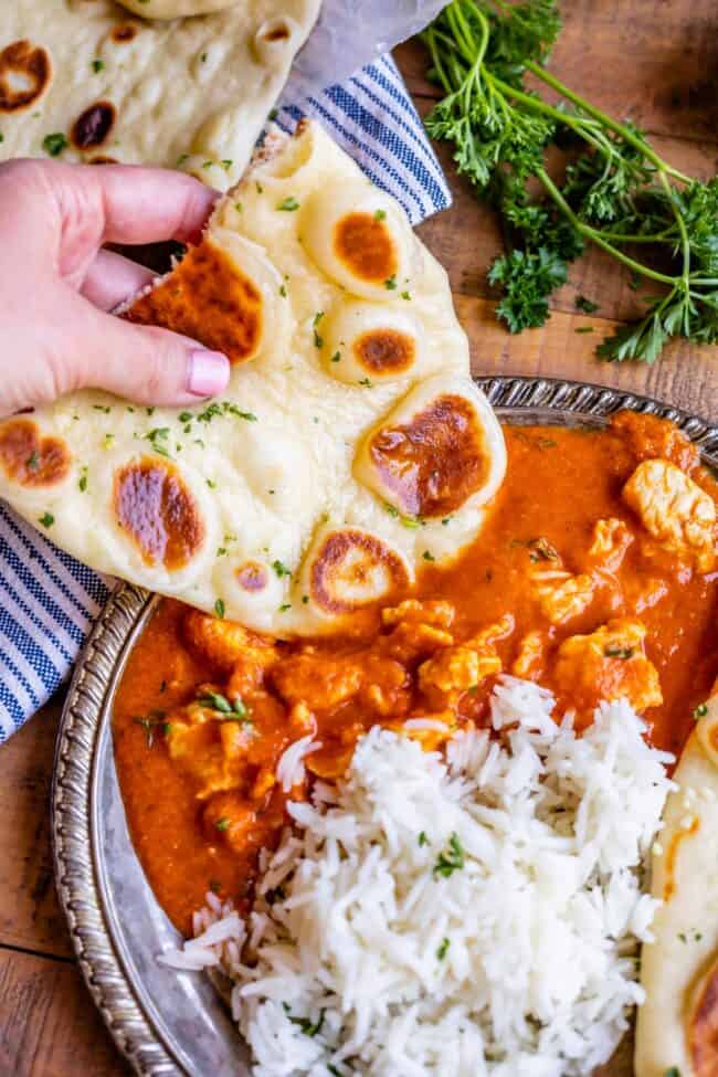 a hand dipping homemade naan into chicken curry next to white rice on a plate.