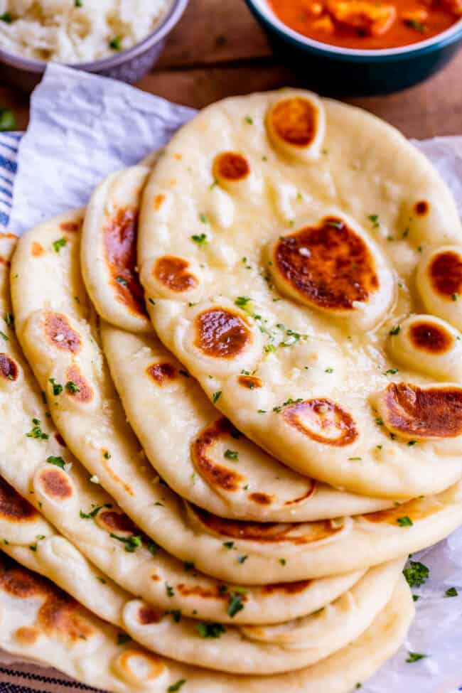 several buttered naan breads on a piece of parchment paper, sprinkled with fresh parsley.