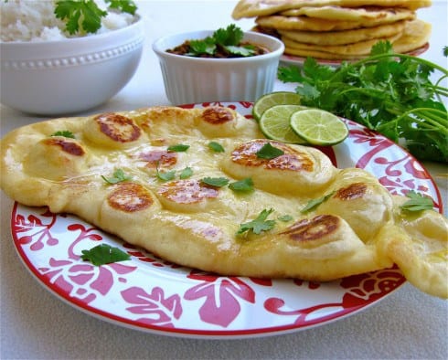 naan with cilantro and lime slices on a red and white plate.