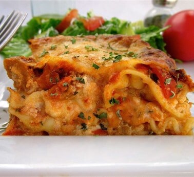 old fashioned lasagna on a white plate with a fork and a side salad.