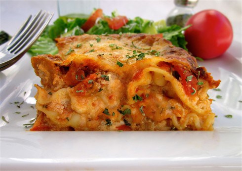 old fashioned lasagna on a white plate with a fork and a side salad.