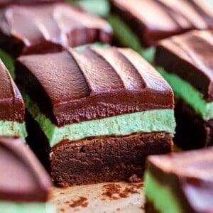 Close-up of mint brownies featuring a fudgy chocolate base, a thick green mint layer, and glossy chocolate ganache, cut into neat squares and arranged on parchment paper.