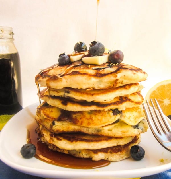 a stack of lemon blueberry pancakes on a white plate with butter and syrup.