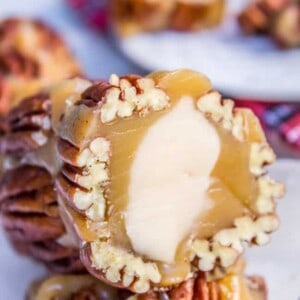 Close-up of pralines with creamy caramel centers and chopped pecans, highlighting their fudge-like texture. A blurred background shows more pralines and a metal spoon.