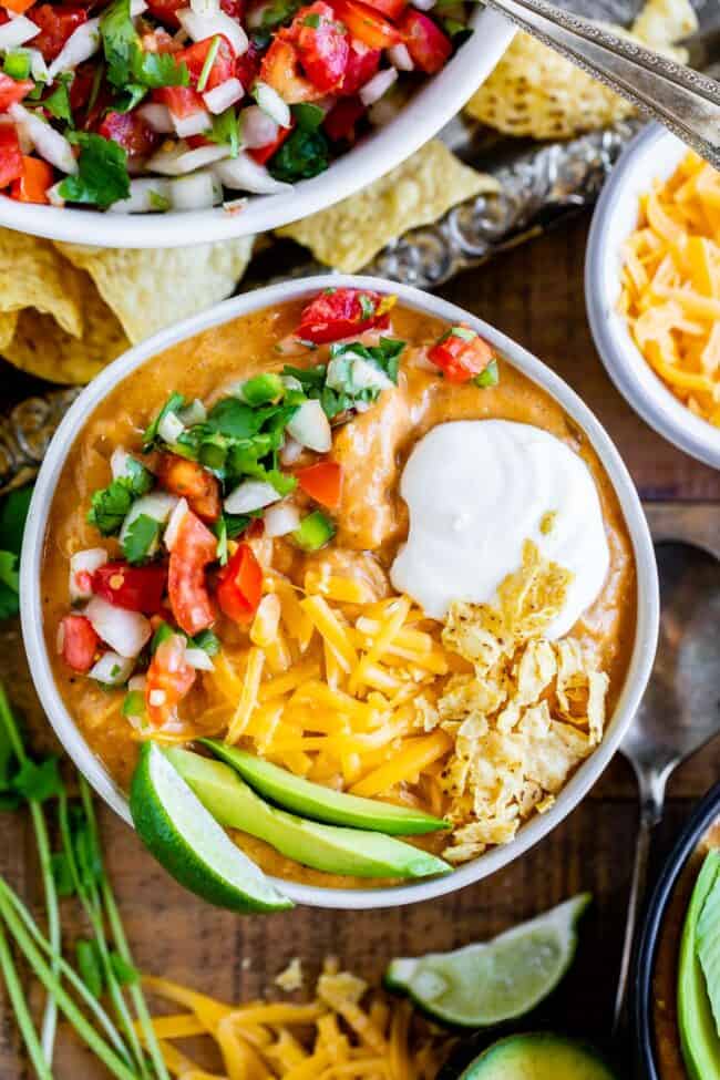 Chili's copycat chicken enchilada soup with pico de gallo, sour cream, chips, cheddar, avocados, and a lime wedge.