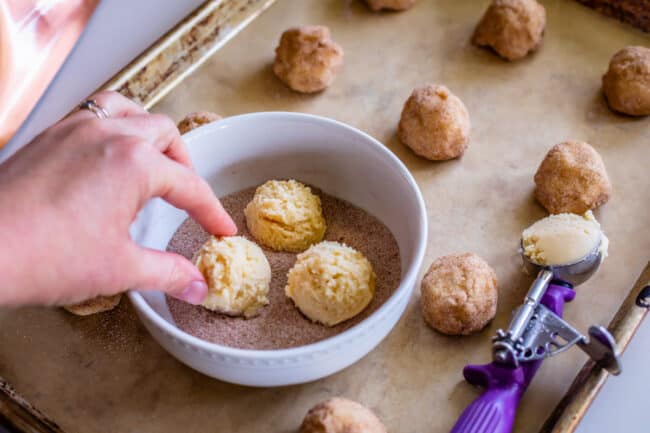 rolling balls of snickerdoodle cookie dough in cinnamon sugar and placing on a pan.