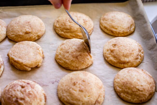 using a spoon to nudge the edge of a cookie on a pan right after baking