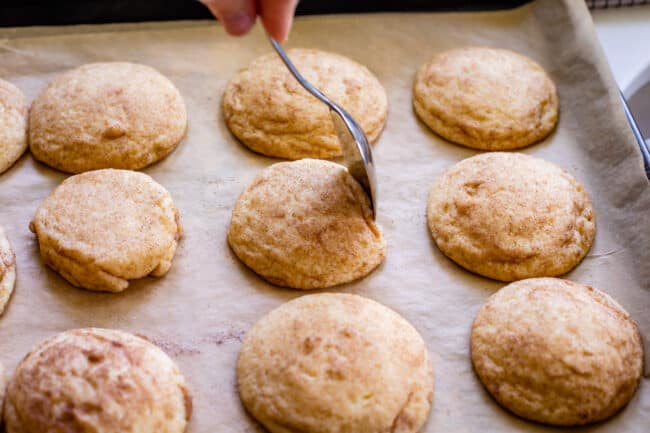 using a spoon to shape the edge of a cookie on a pan right after baking.