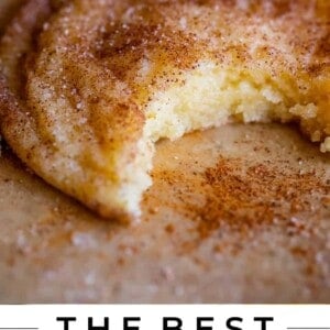 A close-up of a soft, chewy snickerdoodle cookie with a bite taken out, showing its fluffy texture and hint of cinnamon sugar. Text reads: Snickerdoodle Cookies. Soft & Chewy. The Food Charlatan.