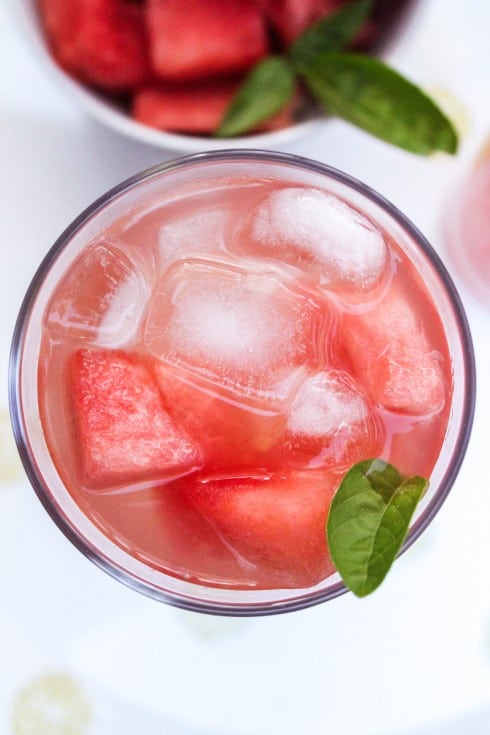 overhead shot of watermelon lemonade in clear glass with ice and basil leaf.