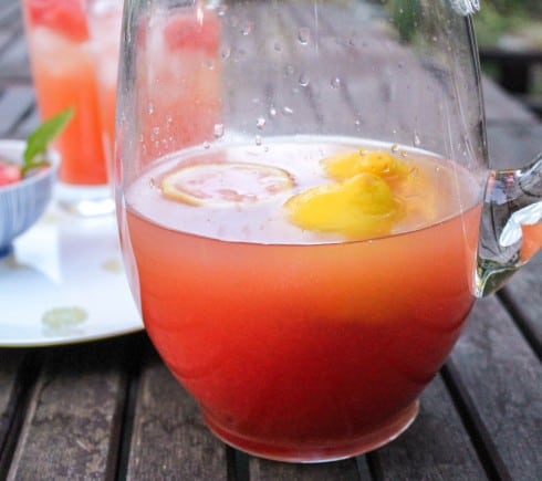 Half full pitcher of bright red watermelon lemonade on a wooden outdoor table.
