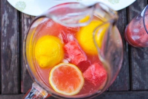 Overhead shot of watermelon lemonade with lemon slices in pitcher on wooden table.